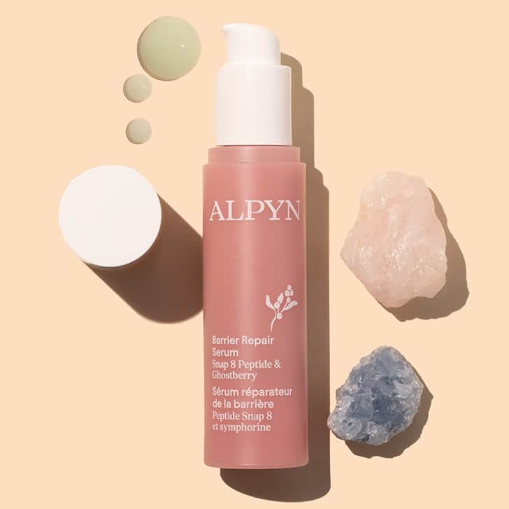 Alpyn Beauty | Barrier Repair Serum | Styled image flat lay with swatch | Pink bottle with white pump and cap and opaque product droplet on peach background