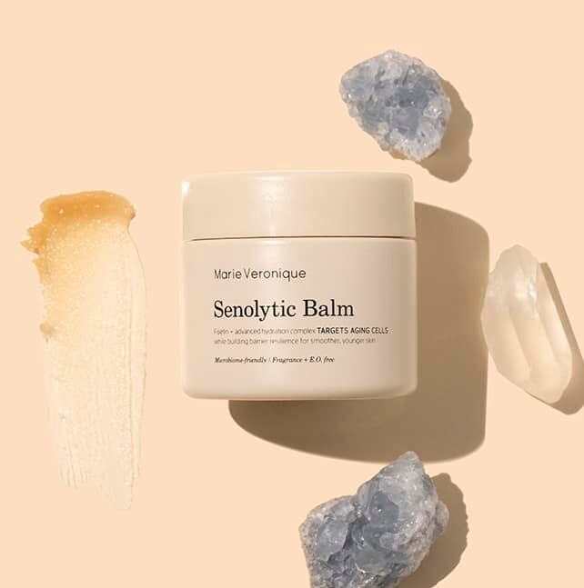 Marie Veronique | Senolytic Balm | Styled Image flat lay with swatch | Beige jar with golden product swatch on peach background with crystals