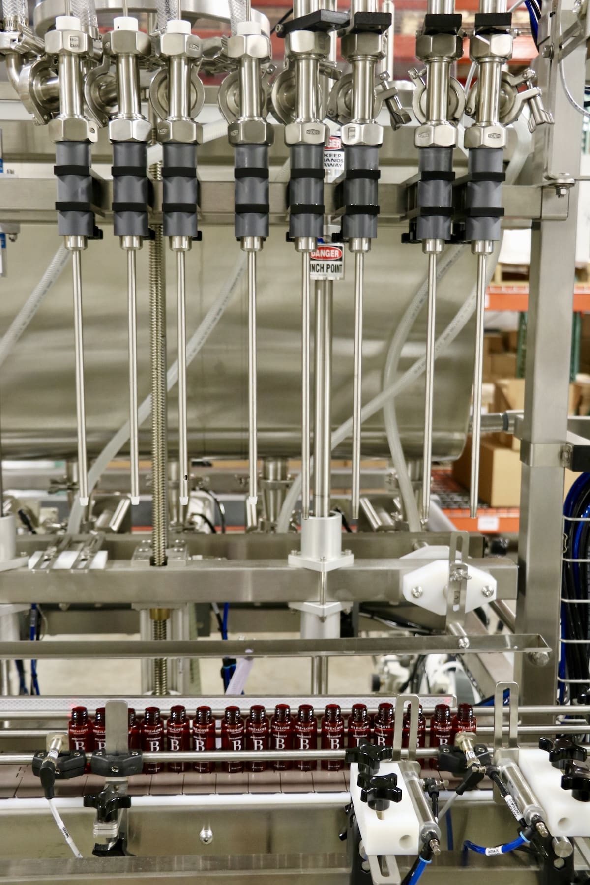High-precision filling machine at One Love Organics' ECOCERT® lab dispensing Botanical B product into glass bottles.